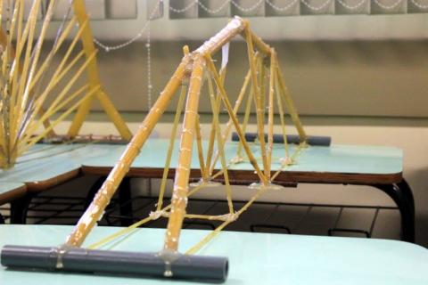 a imagem mostra uma estrutura de ponte em miniatura, feita com massa espaguete, cola epóxi e cola de silicone, depositada sobre uma mesa